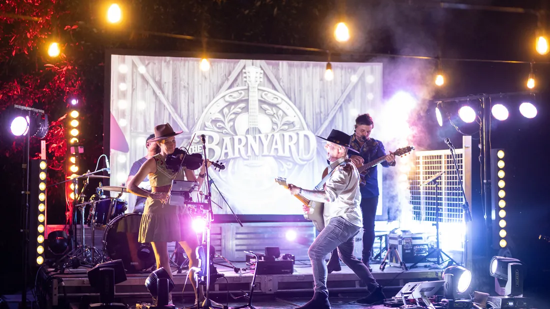 The Barnyard Band on a lit festival stage with the Barnyard logo screen