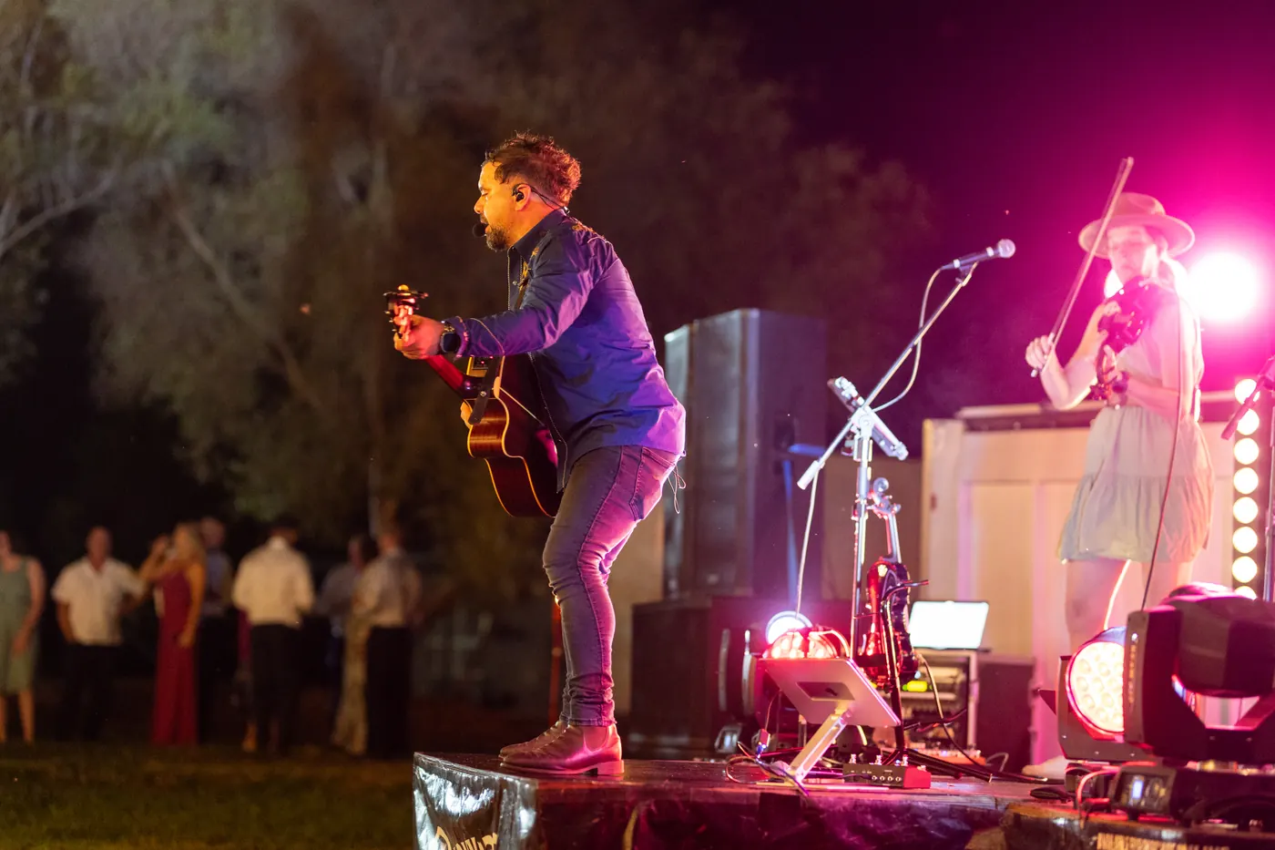 Guitarist and fiddle player on an outdoor stage at night