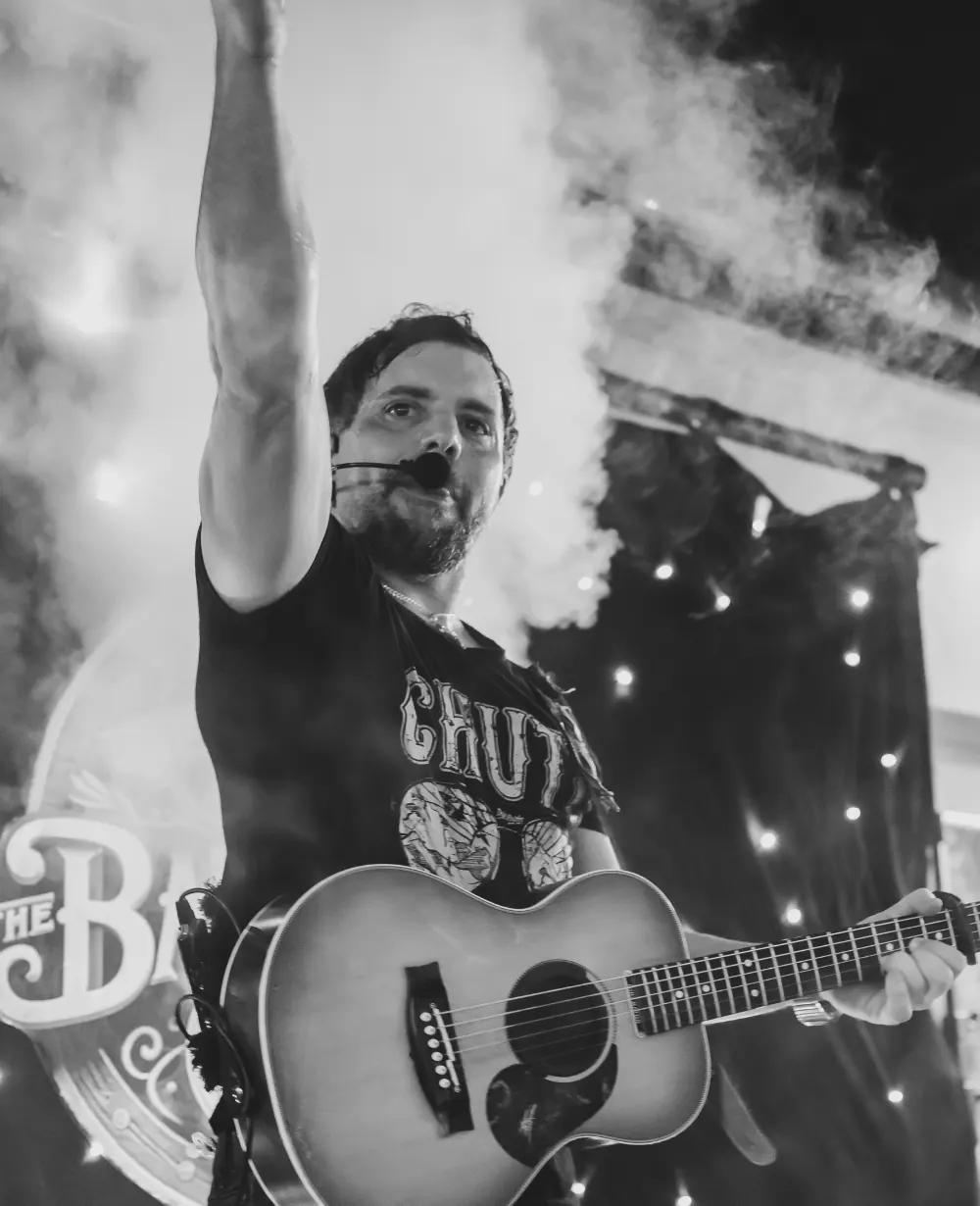 Laurence Sorbello with acoustic guitar, arm raised to the crowd